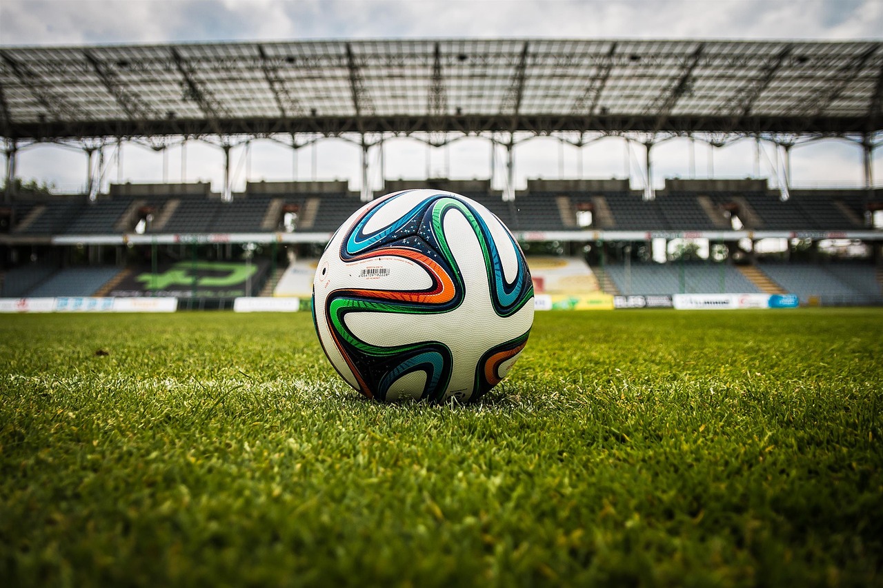A soccer ball resting on the grass of a large, empty stadium.