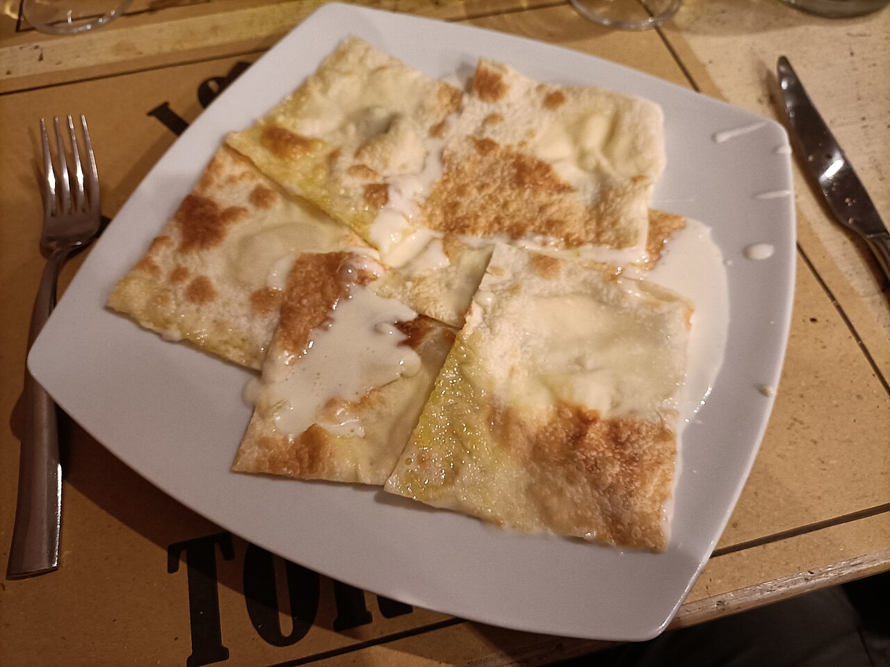 A plate of Focaccia di Recco served on a square white plate with cutlery on the side.