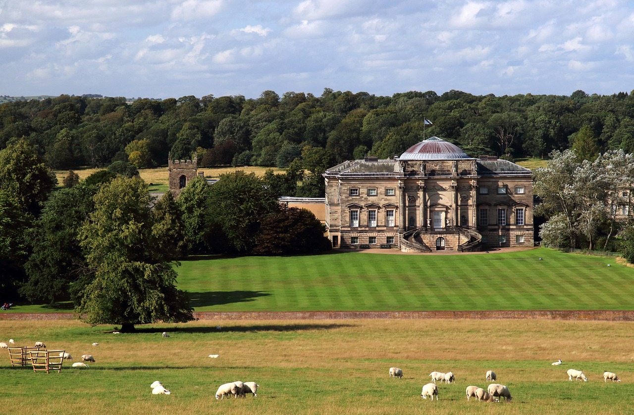 A grand historic English country estate surrounded by green lawns and a field of grazing sheep.