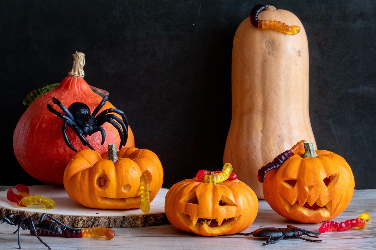 A collection of carved pumpkins, toy spiders, and gummy worms on a wooden surface, representing a Halloween theme.