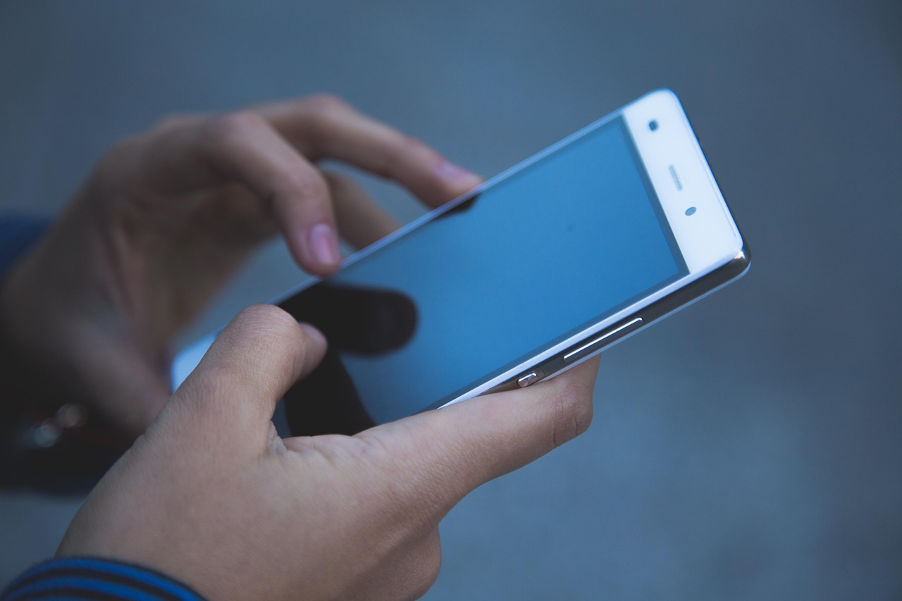 Two hands holding and tapping a smartphone with a blue screen, shown from the side
