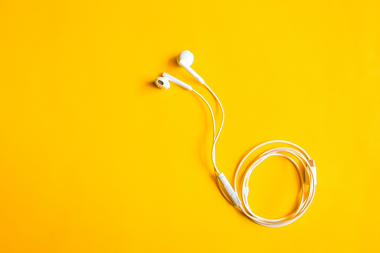A pair of white wired earbuds coiled on a bright yellow background.