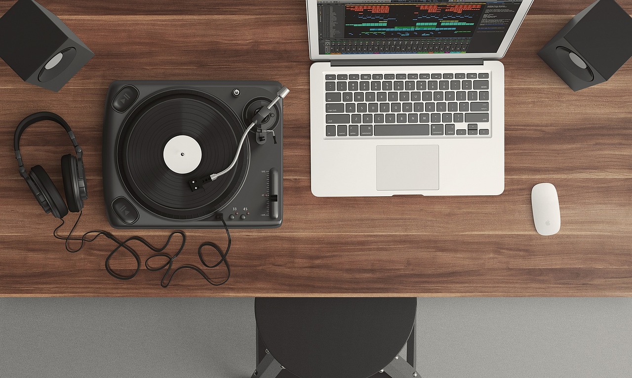 A top-down view of a music production desk featuring a laptop with audio software, a turntable, and headphones.