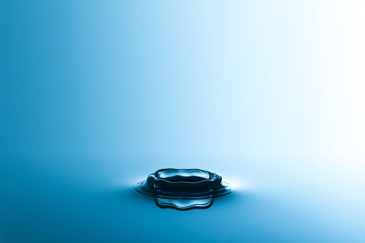 A single water droplet creating a ripple in a blue liquid surface.