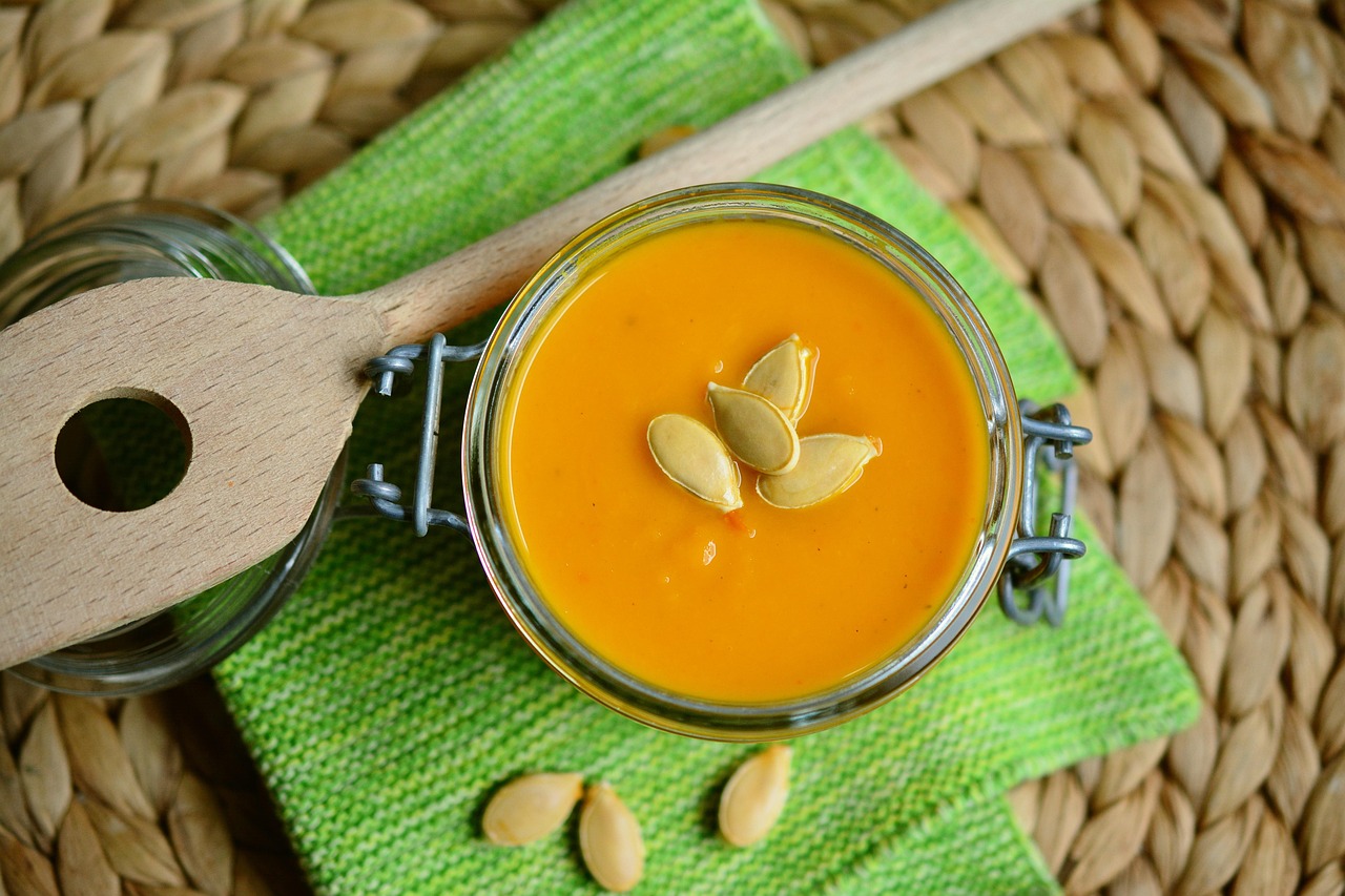 A glass jar filled with orange pumpkin butter, topped with pumpkin seeds, sitting on a green cloth.
