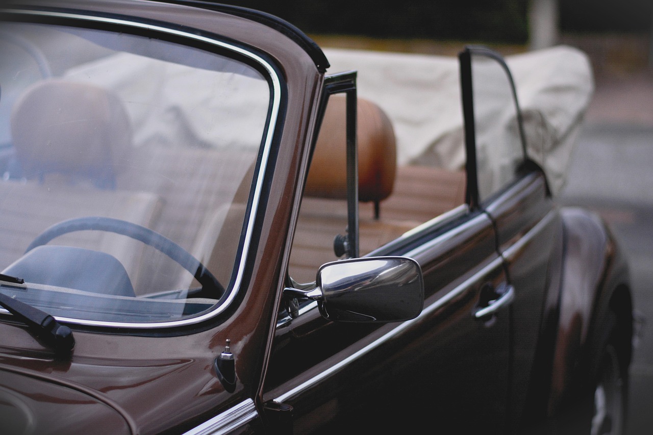 A vintage brown convertible car viewed from the side, showing both the driver's side and the passenger seating area.