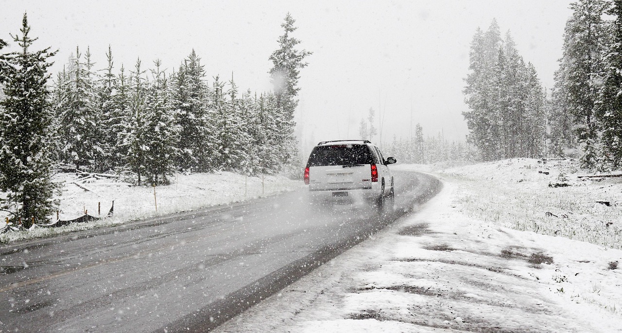 A car driving on a snowy road during a winter storm, representing the conditions where road salt is used.