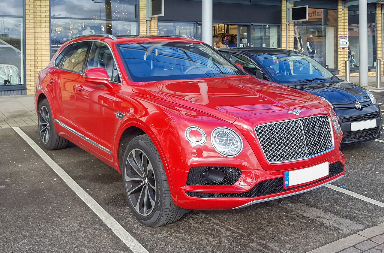 A red Bentley luxury SUV parked in a parking lot, viewed from the front quarter.